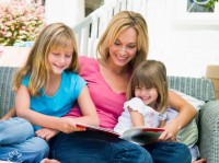 Woman and two young girls sitting on patio reading book smiling